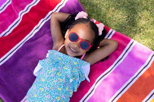 Child wearing sunglasses lying on a towel outside in the sun