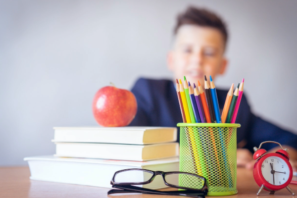Child sitting at a desk with school books, pencils and glasses