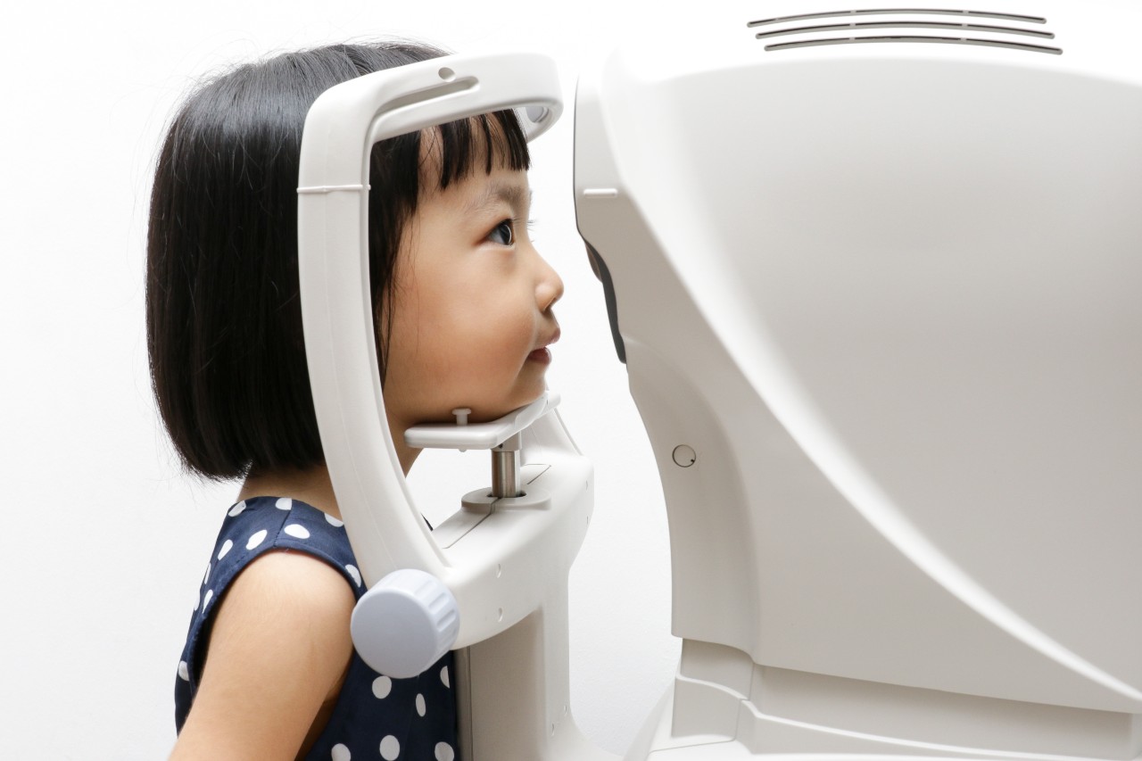 A young girl resting her chin on a machine that measures her eyes during an eye test, seen from the side.