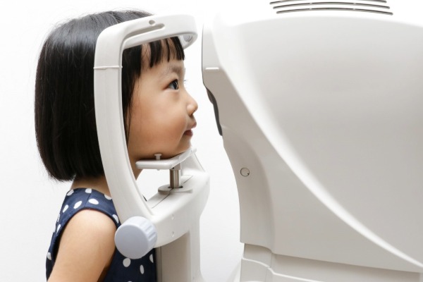A young girl resting her chin on a machine that measures her eyes during an eye test, seen from the side.